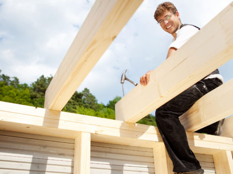 Happy carpenter sitting on the the roof beams and hammering a large nail